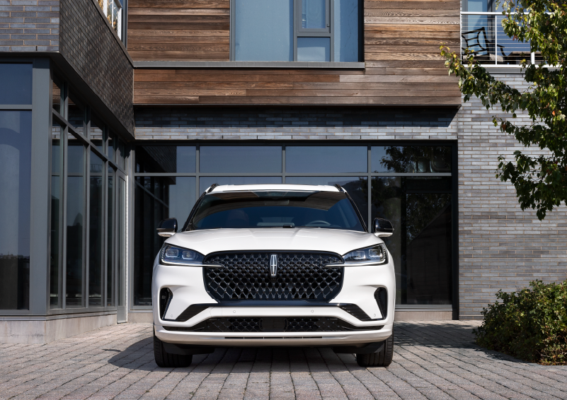 A white 2025 Lincoln Aviator® SUV is shown parked outside a modern building with gray brick and wood accents. | Cummins Lincoln in Weatherford OK