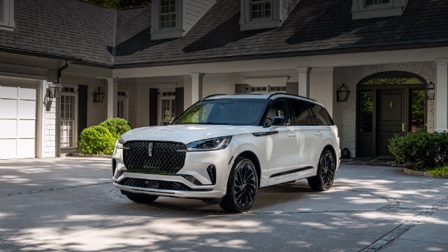 A white 2026 Lincoln Aviator® SUV is parked in the driveway of a luxury home. | Cummins Lincoln in Weatherford OK