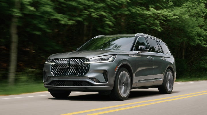 A 2027 Lincoln Aviator® SUV is being driven down a road lined with trees. | Cummins Lincoln in Weatherford OK